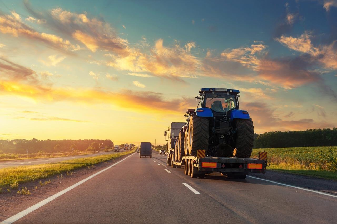 flatbed truck with agriculture equipment driving into sunset
