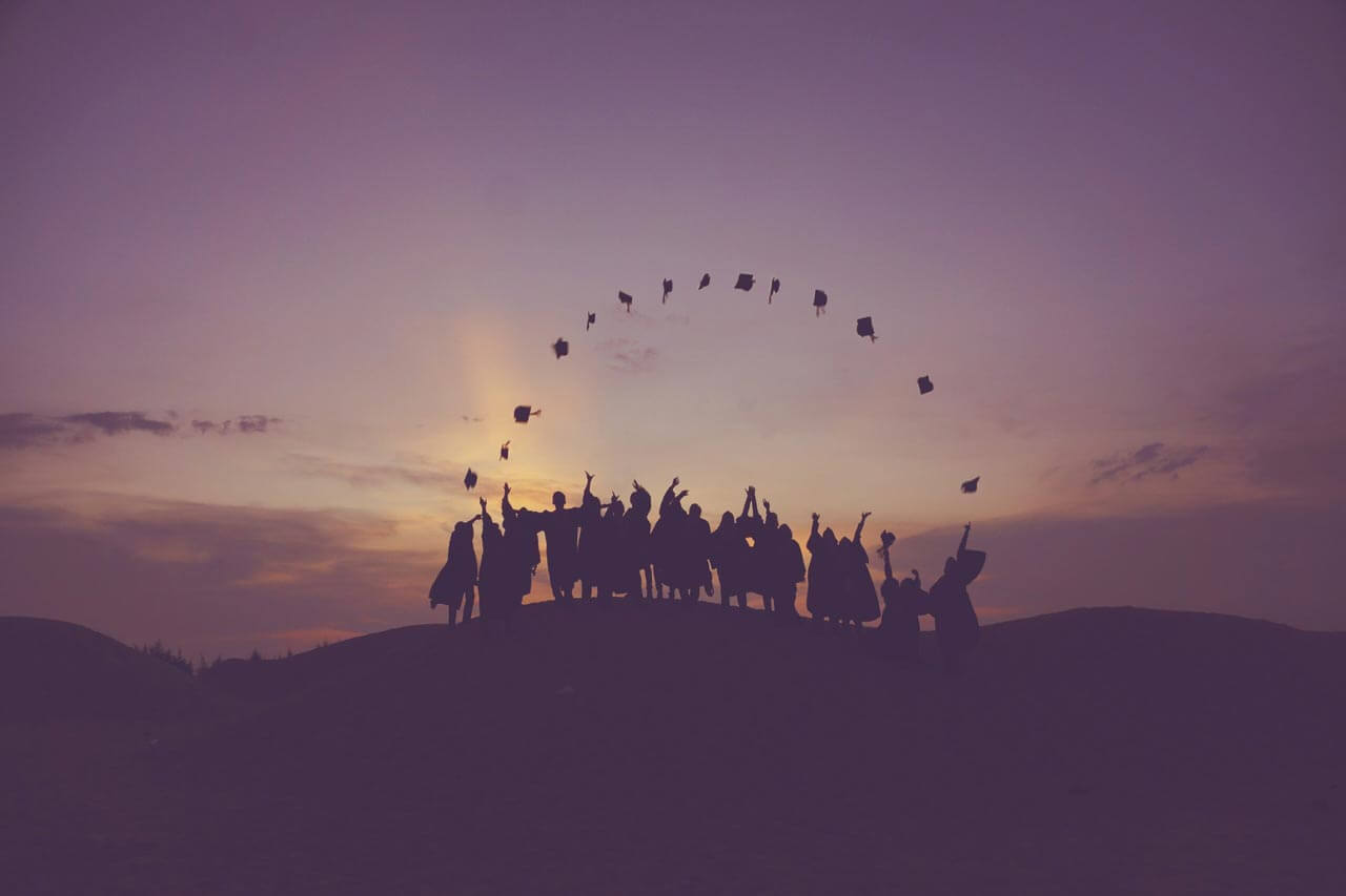 silhouette of graduates on a small hill throwing their graduation caps in the air