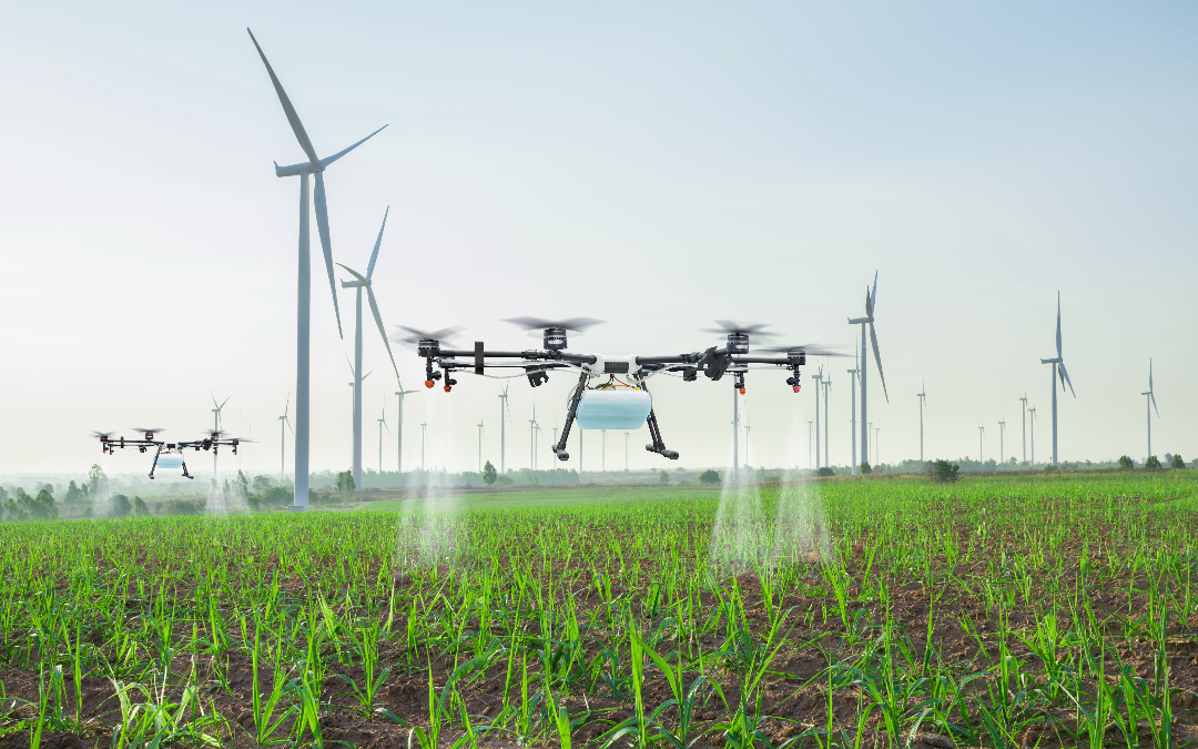 drone spraying liquid on crops with wind turbines behind